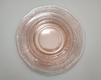May include: A set of four pink glass plates with a delicate floral pattern. The plates are stacked on top of each other, with the largest plate on the bottom and the smallest plate on top.