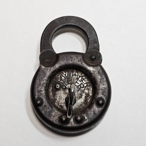 May include: A vintage padlock with a round, black metal body and a keyhole. The padlock has a silver-colored key inserted in the keyhole. The padlock has the text "LYMAN LOCK CO.  NEW YORK" engraved on the front.