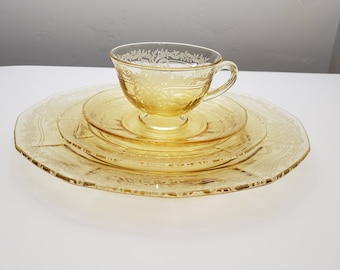 May include: A set of three yellow glass plates with a delicate floral pattern. The set includes a small cup and saucer.