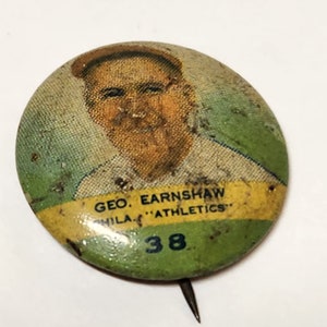 May include: A vintage green and yellow button with a picture of a man and the text "GEO. EARNSHAW PHILA. 'ATHLETICS' 38".