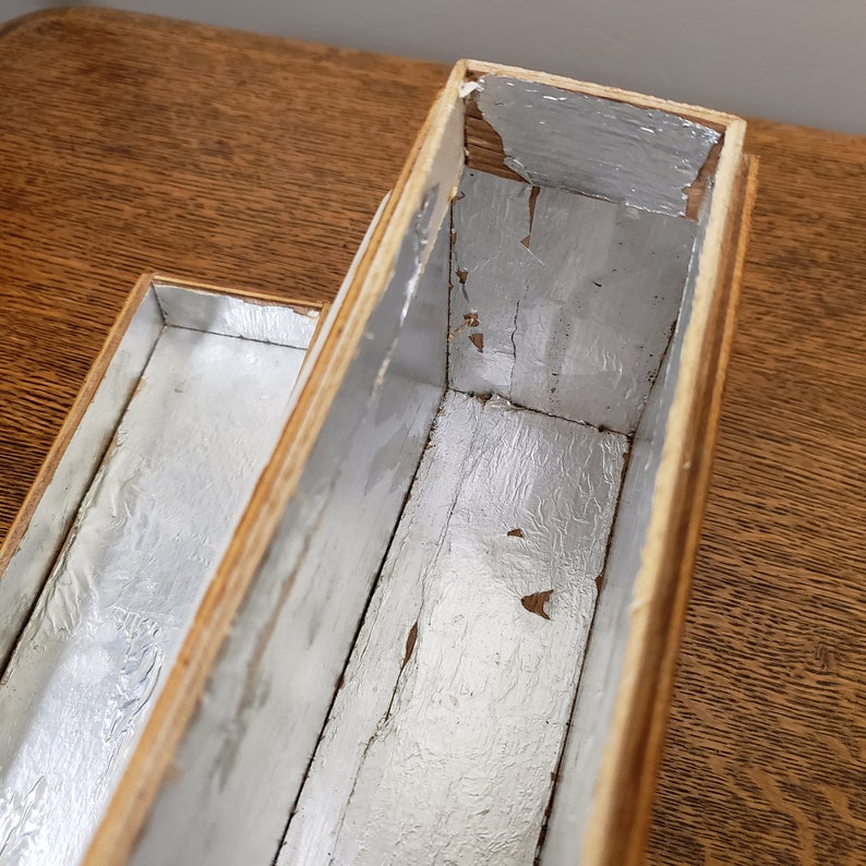 May include: A wooden box with two compartments, each lined with silver foil. The box is made of light wood and has a natural finish.