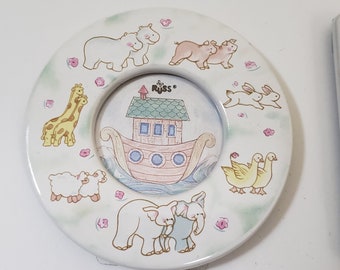 May include: A white ceramic picture frame with a round shape and a raised edge. The frame features a colorful illustration of Noah's Ark with animals, including giraffes, elephants, hippos, pigs, ducks, and rabbits. The frame is decorated with pink flowers and the text "The Russ" is printed on the top of the frame.