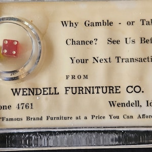 Puede incluir: Una tarjeta blanca con texto negro que dice "Why Gamble - or Take a Chance? See Us Before Your Next Transaction FROM WENDELL FURNITURE CO. Phone 4761 Wendell, Idaho "Famous Brand Furniture at a Price You Can Afford"". Un pequeño contenedor de plástico con dos dados en su interior se encuentra en la esquina superior izquierda de la tarjeta.