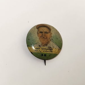 May include: A vintage button featuring a portrait of a baseball player, Geo. Earnshaw, with the text "Phila. "Athletics" 38" underneath.