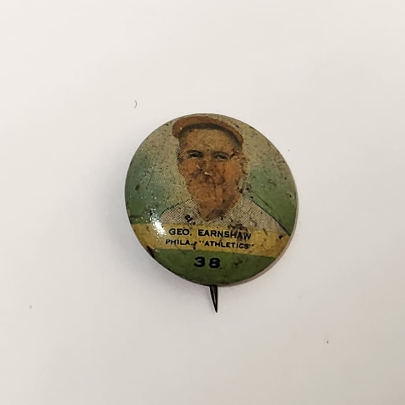 May include: A vintage button featuring a portrait of a baseball player, Geo. Earnshaw, with the text "Phila. "Athletics" 38" underneath.
