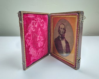 May include: A vintage wooden photo frame with a red velvet interior and a black and white photograph of a man with a beard. The frame has gold accents and a brass clasp.