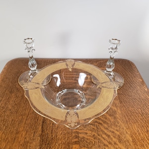 May include: A clear glass bowl with a gold rim and floral design, accompanied by two matching glass candle holders.