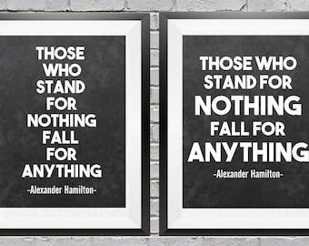 May include: Two black framed prints with white mats on a brick wall. The prints feature a quote by Alexander Hamilton: "Those who stand for nothing fall for anything."