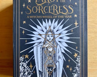 May include: A black rectangular tarot deck box titled Tarot of the Sorceress: A Witch's Wheel of the Year by Bérengère Demoncy. The cover features gold foil text and star accents, with a central black and white illustration of a figure.