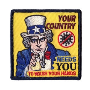 Puede incluir: Un parche bordado amarillo y azul con el Tío Sam sosteniendo una botella de desinfectante para manos. El texto dice "Tu país te necesita para lavarte las manos".