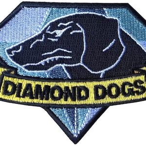 Op de afbeelding: Een geborduurde zwarte en gele patch in de vorm van een diamant. De patch heeft een zwart hondenhoofd met een witte omtrek en de tekst "DIAMOND DOGS" in zwarte letters op een gele banner.