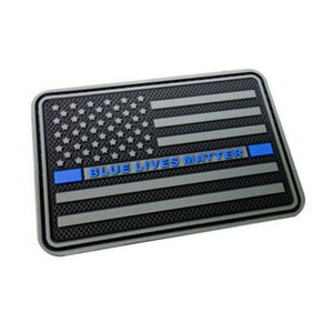 Puede incluir: Un parche de bandera estadounidense gris y negro con una franja azul en la parte inferior y el texto "BLUE LIVES MATTER" en letras azules.