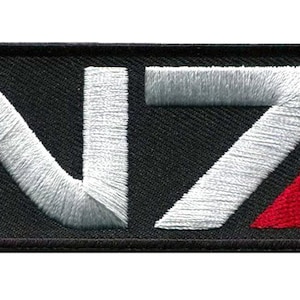 Könnte beinhalten: Ein rechteckiger, bestickter Aufnäher mit schwarzem Hintergrund, weiß gesticktem N7-Schriftzug und einem roten Dreieck auf der rechten Seite. Das Design ist von einem schwarzen, gestickten Rand umgeben, der für einen sauberen Abschluss sorgt.