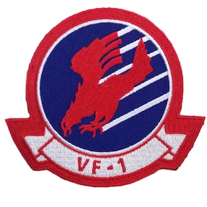 Op de afbeelding: Geborduurde patch met een rode roofvogel op een blauwe achtergrond, omlijst door een rode en witte rand. De tekst "VF-1" staat op een witte banner. Waarschijnlijk een militair of luchtvaartembleem.