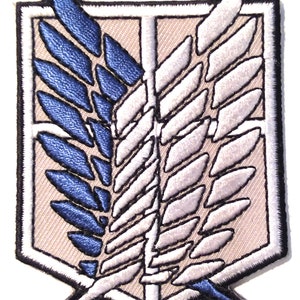 Puede incluir: Un parche bordado blanco y azul con un símbolo alado, que se asemeja a un ave rapaz estilizada, dentro de una forma de escudo bordeada de blanco. Las alas se cruzan en el centro, una blanca y la otra azul.