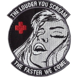 Peut inclure: Un écusson brodé noir et blanc avec le visage d'une femme et le texte "The Louder You Scream The Faster We Come" dans un cercle blanc. Une croix médicale rouge se trouve dans le coin supérieur gauche.
