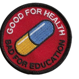Op de afbeelding: Een rood geborduurd patch met zwarte stiksels. De patch heeft een witte pil met een gele en blauwe capsule. De tekst rond de pil luidt "Goed voor de gezondheid Slecht voor onderwijs".