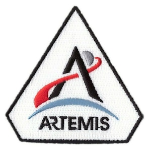 Könnte beinhalten: Ein weißer dreieckiger Patch mit schwarzem Rand und einem schwarzen Buchstaben "A" mit einer roten und blauen geschwungenen Linie darum. Der Text "ARTEMIS" befindet sich unter dem Buchstaben "A".