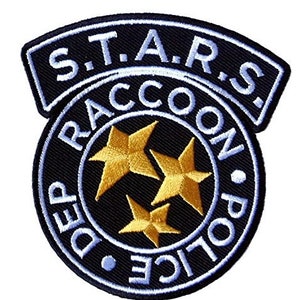 May include: A circular embroidered patch featuring a black background with three gold stars in the centre. The text S.T.A.R.S. is arched at the top, while RACCOON POLICE DEP is written in a circular border around the stars in light blue lettering.
