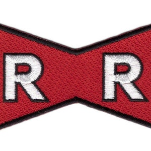 Op de afbeelding: Een vlinderdasvormige geborduurde patch met een felrode achtergrond en een dikke zwarte rand. Twee grote, vetgedrukte, witte hoofdletters R zijn op de linker- en rechterkant van de rode stof geborduurd, wat een opvallend grafisch ontwerp vormt.