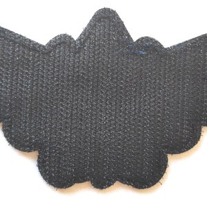May include: Black felt patch with a scalloped edge in the shape of wings.