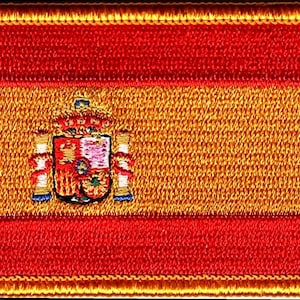 Op de afbeelding: Geborduurde patch met de Spaanse vlag. Het ontwerp bestaat uit drie horizontale strepen: twee rode strepen aan de boven- en onderkant en een bredere gele streep in het midden. Het Spaanse wapen staat in het midden van de gele streep.