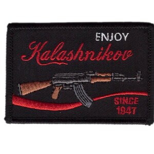Könnte beinhalten: Schwarzer, gestickter Aufnäher mit einem Gewehrdesign und den Worten "Enjoy Kalashnikov" in roter Schrift. Der Text "Since 1947" ist ebenfalls in Rot enthalten. Der Aufnäher hat eine rechteckige Form.