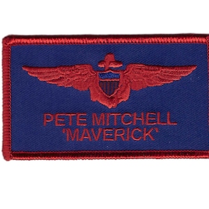 May include: Red embroidered name tag with a blue background. The tag features a red pilot wings emblem with a shield and the text "Pete Mitchell 'Maverick'".