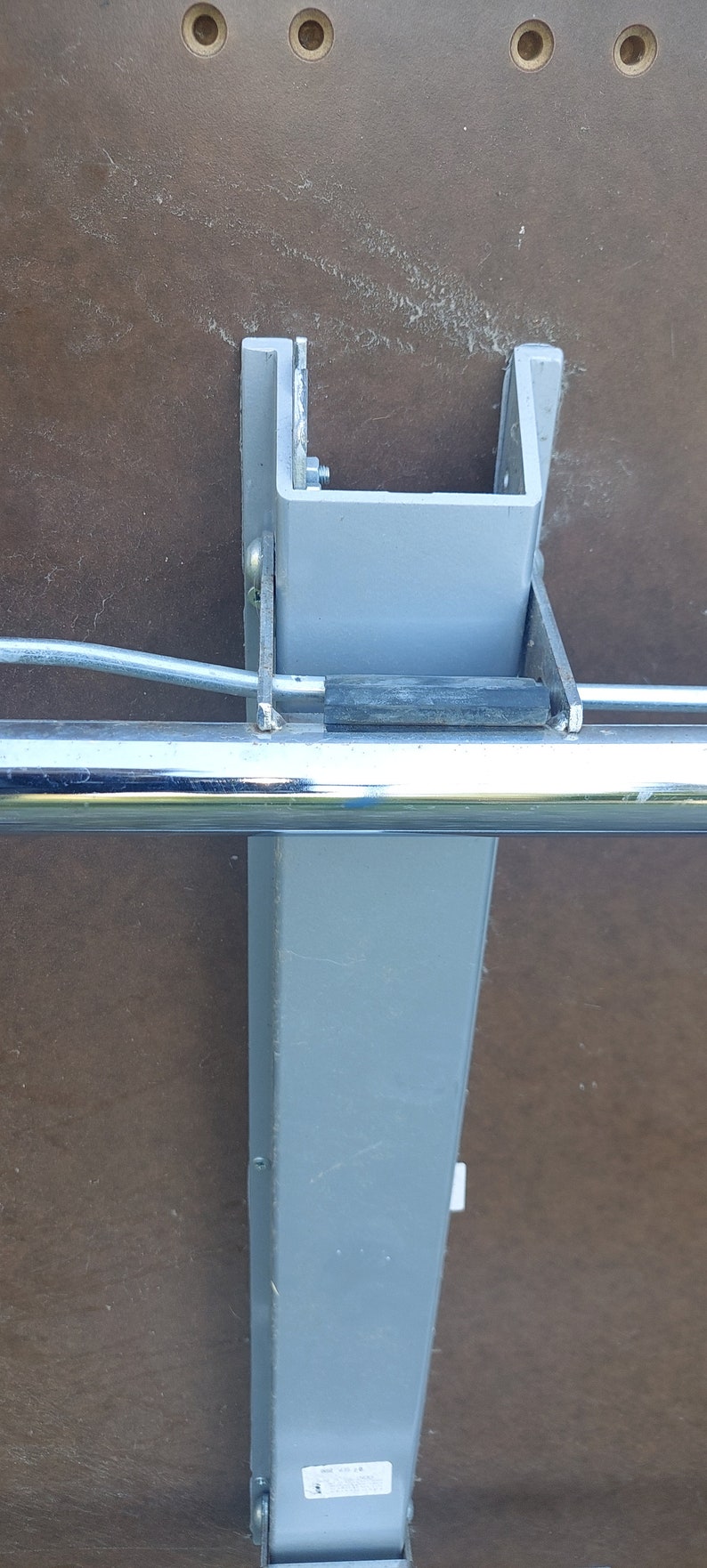 Może przedstawiać: Zbliżenie na szarą metalową nogę stołu z przymocowaną chromowaną belką. Noga ma etykietę z tekstem "Made in China".