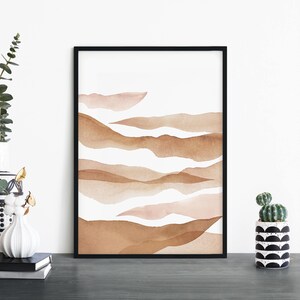 May include: Abstract watercolor print with a black frame. The print features a series of overlapping brown and pink watercolor shapes that resemble hills or waves.