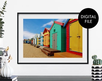 May include: A row of colorful beach huts with bright blue, red, yellow, green, and orange paint. The huts are lined up on a sandy beach with a blue sky in the background.