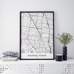 Puede incluir: Una impresión enmarcada en negro de un mapa de Moonee Ponds, VIC 3039. El mapa está en blanco y negro con acentos rosados. La impresión está en un estante blanco con un jarrón negro y un tazón negro.