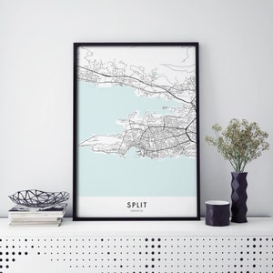 May include: A black and white map print of Split, Croatia, in a black frame. The map shows the city's streets and coastline. The print is on a white background with a light blue colour representing the water.