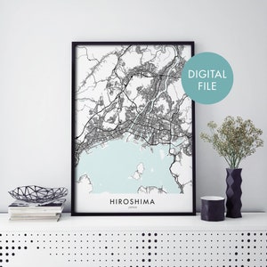 Puede incluir: Mapa de líneas en blanco y negro de Hiroshima, Japón, en un marco negro. El mapa muestra las calles, las vías fluviales y las áreas circundantes de la ciudad. El texto "HIROSHIMA" y "JAPÓN" está impreso debajo del mapa.