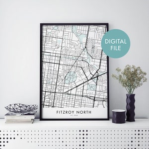 May include: A black and white map print of Fitzroy North, VIC 3068, Australia, in a black frame. The map is printed on white paper and shows the streets and landmarks of the area. The print is labeled "Fitzroy North" and "VIC 3068" in black text. The print is displayed on a white shelf with a black and white patterned background.