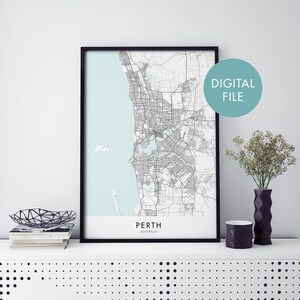 Puede incluir: Un mapa en blanco y negro de Perth, Australia, en un marco negro. El mapa está impreso en papel blanco con un fondo azul claro. El texto "PERTH" y "AUSTRALIA" está impreso en negro en la parte inferior del mapa. Las palabras "DIGITAL FILE" están impresas en blanco sobre un círculo azul claro en la esquina superior derecha de la imagen.