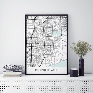 Puede incluir: Una impresión enmarcada en negro de un mapa de Morphett Vale, Australia del Sur. El mapa está en blanco y negro con una característica de agua azul claro. El texto "Morphett Vale" y "SA 5162" está impreso debajo del mapa.