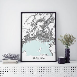 Puede incluir: Impresión de mapa en blanco y negro de Hiroshima, Japón, en un marco negro. El mapa muestra las calles y vías fluviales de la ciudad. El nombre de la ciudad está impreso debajo del mapa.