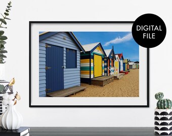 May include: A row of colorful beach huts with blue, yellow, green, and red paint. The huts are lined up on a sandy beach with a blue sky and white clouds in the background.