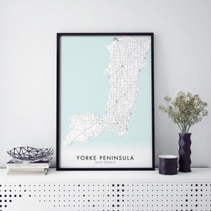 Puede incluir: Una impresión enmarcada en negro de un mapa de la península de Yorke en Australia del Sur. El mapa está sobre un fondo azul claro y muestra las carreteras y las ciudades de la península. El texto "Yorke Peninsula, South Australia" está impreso debajo del mapa.