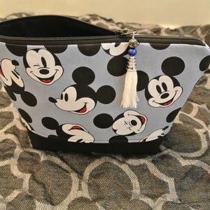 May include: A blue and black zippered pouch with a Mickey Mouse print. The pouch has a white tassel with a blue and silver bead.