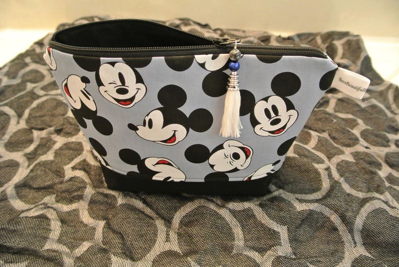 May include: A blue and black zippered pouch with a Mickey Mouse print. The pouch has a white tassel with a blue and silver bead.