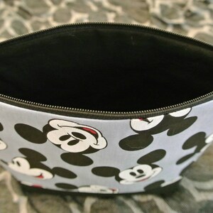 May include: A blue and black zippered pouch with a repeating pattern of Mickey Mouse heads. The pouch is open and the inside is black.