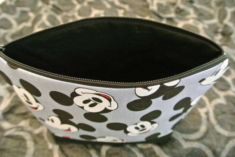 May include: A blue and black zippered pouch with a repeating pattern of Mickey Mouse heads. The pouch is open and the inside is black.
