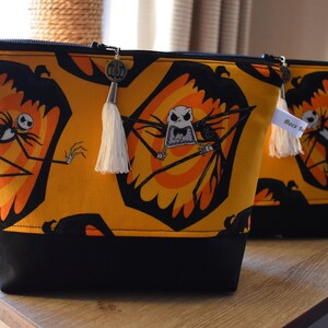 May include: Two black and yellow zippered pouches with a black and white Jack Skellington print. The pouches have black fabric bottoms and white tassels.