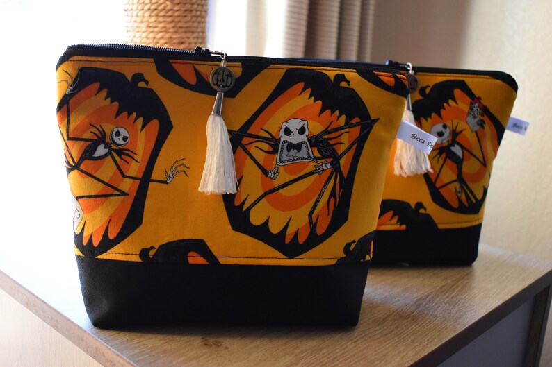 May include: Two black and yellow zippered pouches with a black and white Jack Skellington print. The pouches have black fabric bottoms and white tassels.