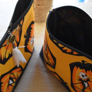 May include: Two yellow and black zippered pouches with a white tassel. One pouch is open and shows a black interior. The pouch has a black and orange print of Jack Skellington from The Nightmare Before Christmas.