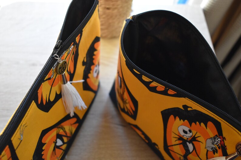 May include: Two yellow and black zippered pouches with a white tassel. One pouch is open and shows a black interior. The pouch has a black and orange print of Jack Skellington from The Nightmare Before Christmas.