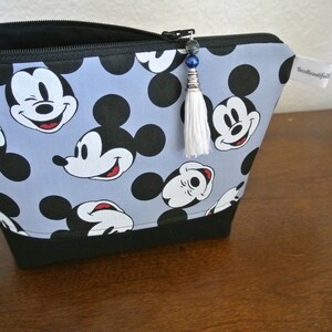 May include: A blue and black zippered pouch with a white tassel. The pouch is decorated with a repeating pattern of Mickey Mouse heads.