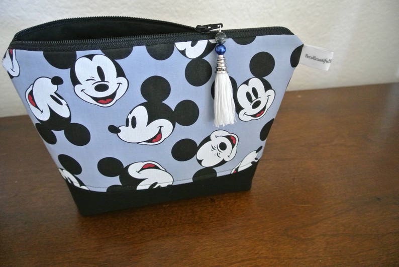 May include: A blue and black zippered pouch with a white tassel. The pouch is decorated with a repeating pattern of Mickey Mouse heads.